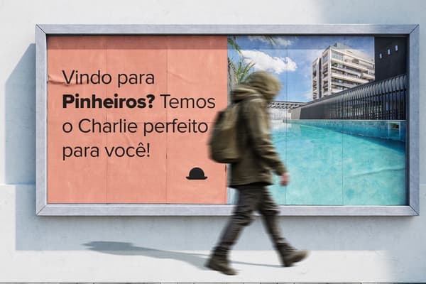 Um outdoor exibe um anúncio dividido. À esquerda, em um fundo cor salmão, o texto "Vindo para Pinheiros? Temos o Charlie perfeito para você!" e um ícone de chapéu coco preto. À direita, uma piscina azul vibrante com espreguiçadeiras e um prédio moderno ao fundo. Um pedestre borrado caminha à frente do outdoor, ilustrando categoria de short e long stay em Pinheiros